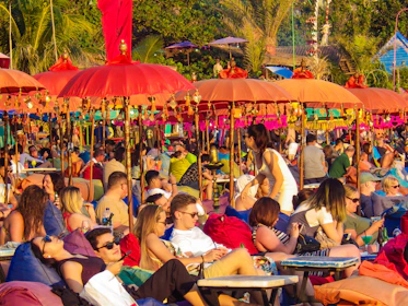 Group of friends enjoying a lively beach picnic with music and laughter under palm trees.
