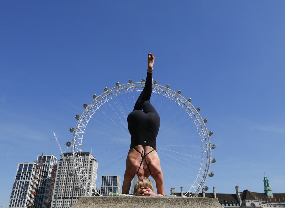 a woman doing a handstand in front of a ferris wheel