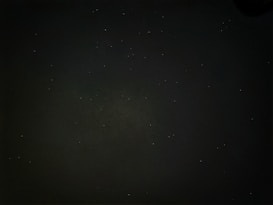 A dark night sky filled with numerous small bright stars spread across the scene. The background is predominantly black with a faint hint of dark green, creating a serene and infinite atmosphere.