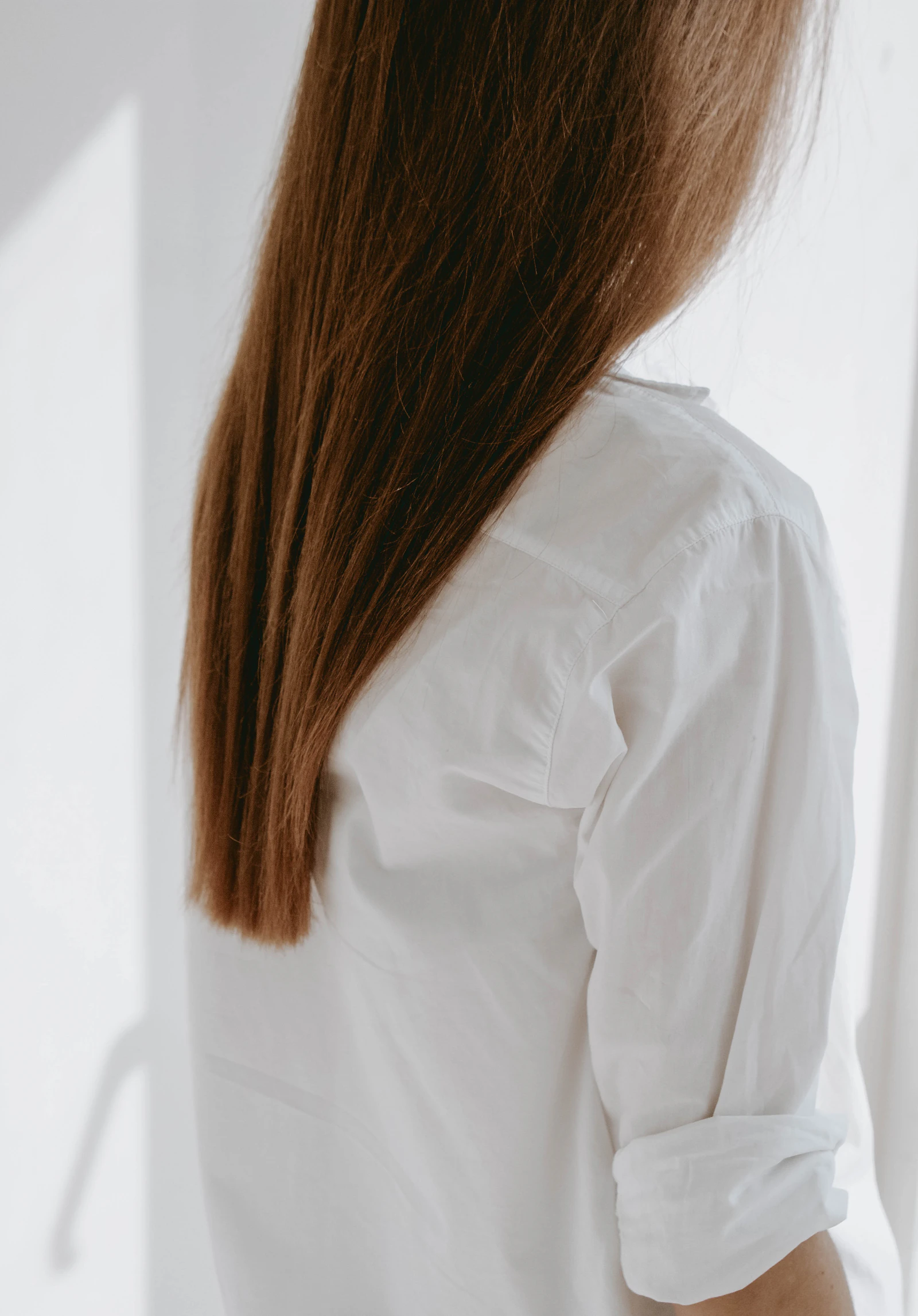 Long smooth hair falling over the shoulder of a white shirt in soft daylight