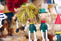 Several colorful, wooden marionette dolls are hanging on display. Each is crafted with unique features, such as bright yarn hair, expressive painted faces, and playful outfits, including hats and accessories.