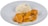 A dish featuring a serving of white rice paired with a portion of chicken covered in an orange, creamy sauce. The sauce is garnished with herbs and spices, possibly including cardamom pods and cloves. The presentation is on a simple white plate.