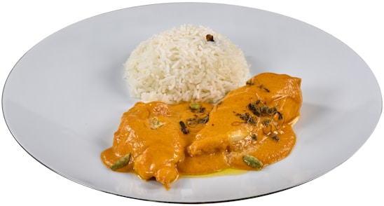 A dish featuring a serving of white rice paired with a portion of chicken covered in an orange, creamy sauce. The sauce is garnished with herbs and spices, possibly including cardamom pods and cloves. The presentation is on a simple white plate.