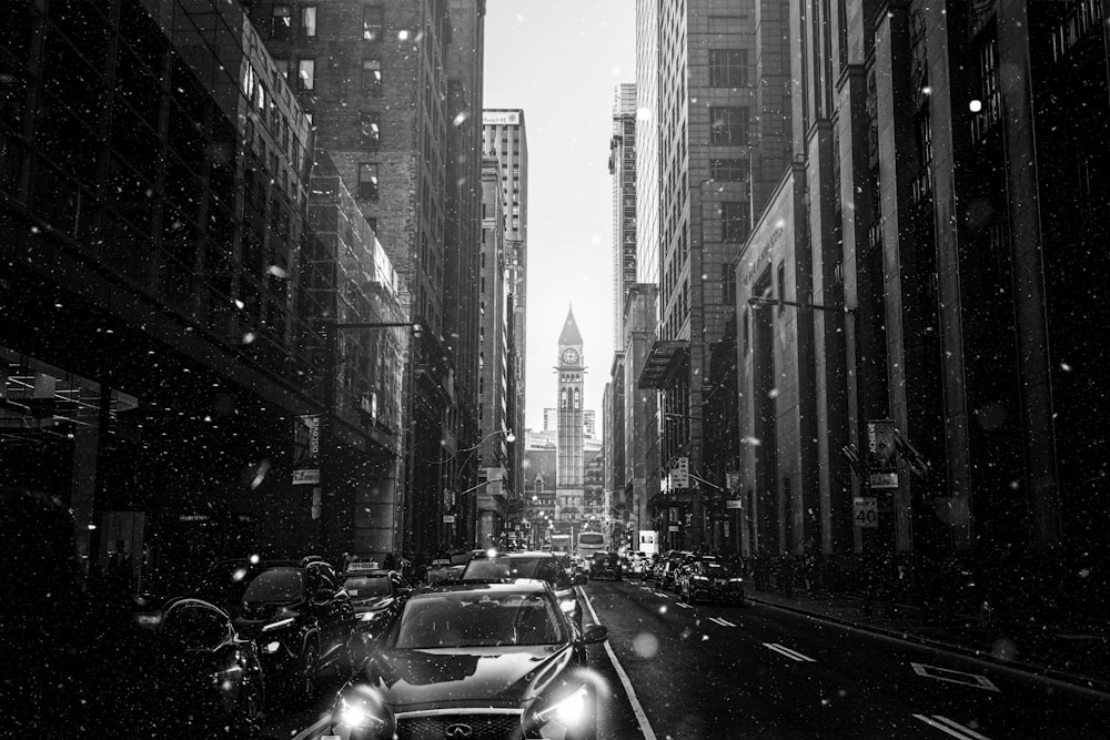 grayscale photography of people walking on pathway near buildings and different vehicles on road