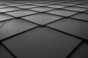 A grid pattern consisting of square tiles with slightly beveled edges, creating a sense of depth and perspective. The surface appears smooth with some small scratches or marks visible.
