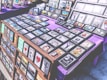 A marketplace stall features an array of framed images and posters with various designs, arranged on tables covered with purple cloth. The collection includes diverse themes such as landscapes, inspirational quotes, pop culture references, and abstract art. The frames are neatly organized, and some larger prints are displayed upright in the background.