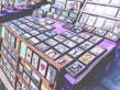 A marketplace stall features an array of framed images and posters with various designs, arranged on tables covered with purple cloth. The collection includes diverse themes such as landscapes, inspirational quotes, pop culture references, and abstract art. The frames are neatly organized, and some larger prints are displayed upright in the background.