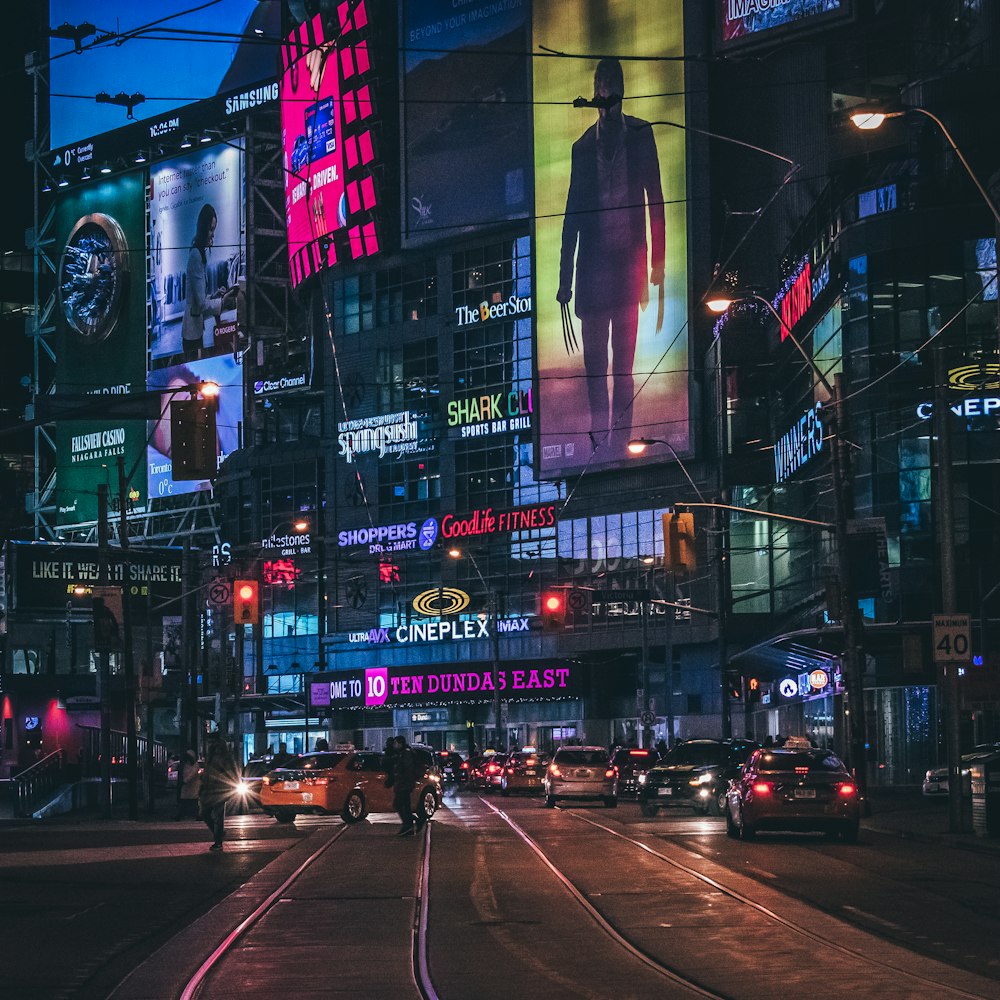 people walking on pathway near buildings and different vehicles on road during night time