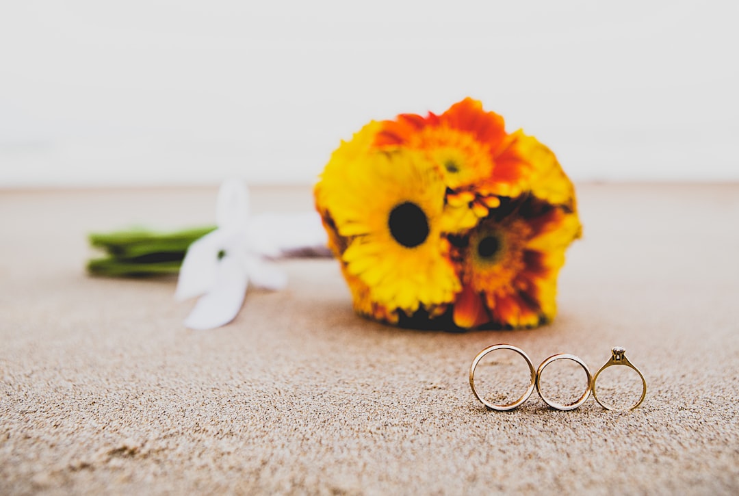gold-colored wedding ring set beside bouquet of flowers
