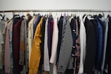 A clothing rack filled with a variety of garments, including shirts, jackets, and blazers in different colors and patterns. The assortment displays a diverse selection of fabrics and designs, indicating a collection of formal and casual wear.