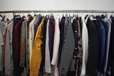 A clothing rack filled with a variety of garments, including shirts, jackets, and blazers in different colors and patterns. The assortment displays a diverse selection of fabrics and designs, indicating a collection of formal and casual wear.