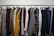 A clothing rack filled with a variety of garments, including shirts, jackets, and blazers in different colors and patterns. The assortment displays a diverse selection of fabrics and designs, indicating a collection of formal and casual wear.