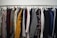 A clothing rack filled with a variety of garments, including shirts, jackets, and blazers in different colors and patterns. The assortment displays a diverse selection of fabrics and designs, indicating a collection of formal and casual wear.