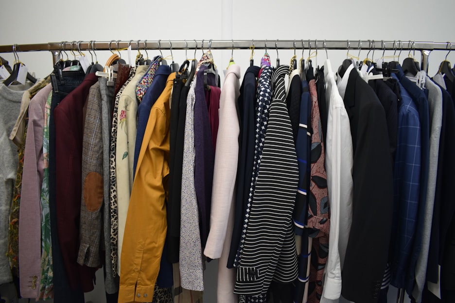 A clothing rack filled with a variety of garments, including shirts, jackets, and blazers in different colors and patterns. The assortment displays a diverse selection of fabrics and designs, indicating a collection of formal and casual wear.