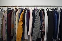 A clothing rack filled with a variety of garments, including shirts, jackets, and blazers in different colors and patterns. The assortment displays a diverse selection of fabrics and designs, indicating a collection of formal and casual wear.