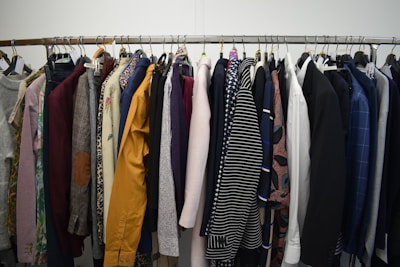 A clothing rack filled with a variety of garments, including shirts, jackets, and blazers in different colors and patterns. The assortment displays a diverse selection of fabrics and designs, indicating a collection of formal and casual wear.