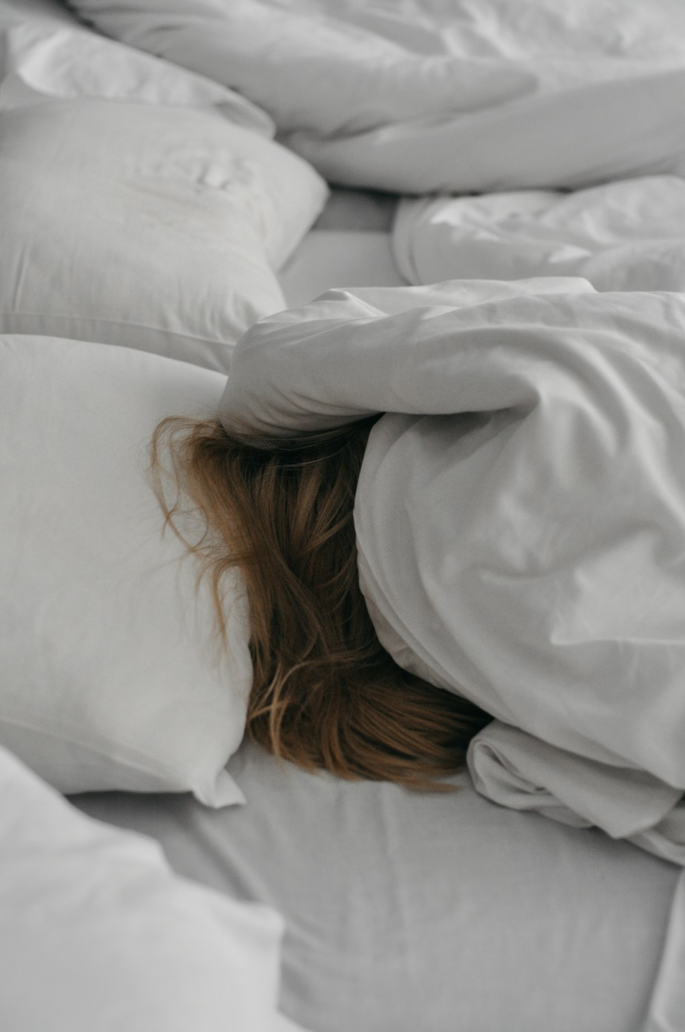 a woman is hiding under a blanket on a bed