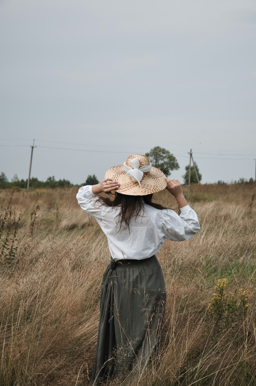woman standing and touching her hat on grass field