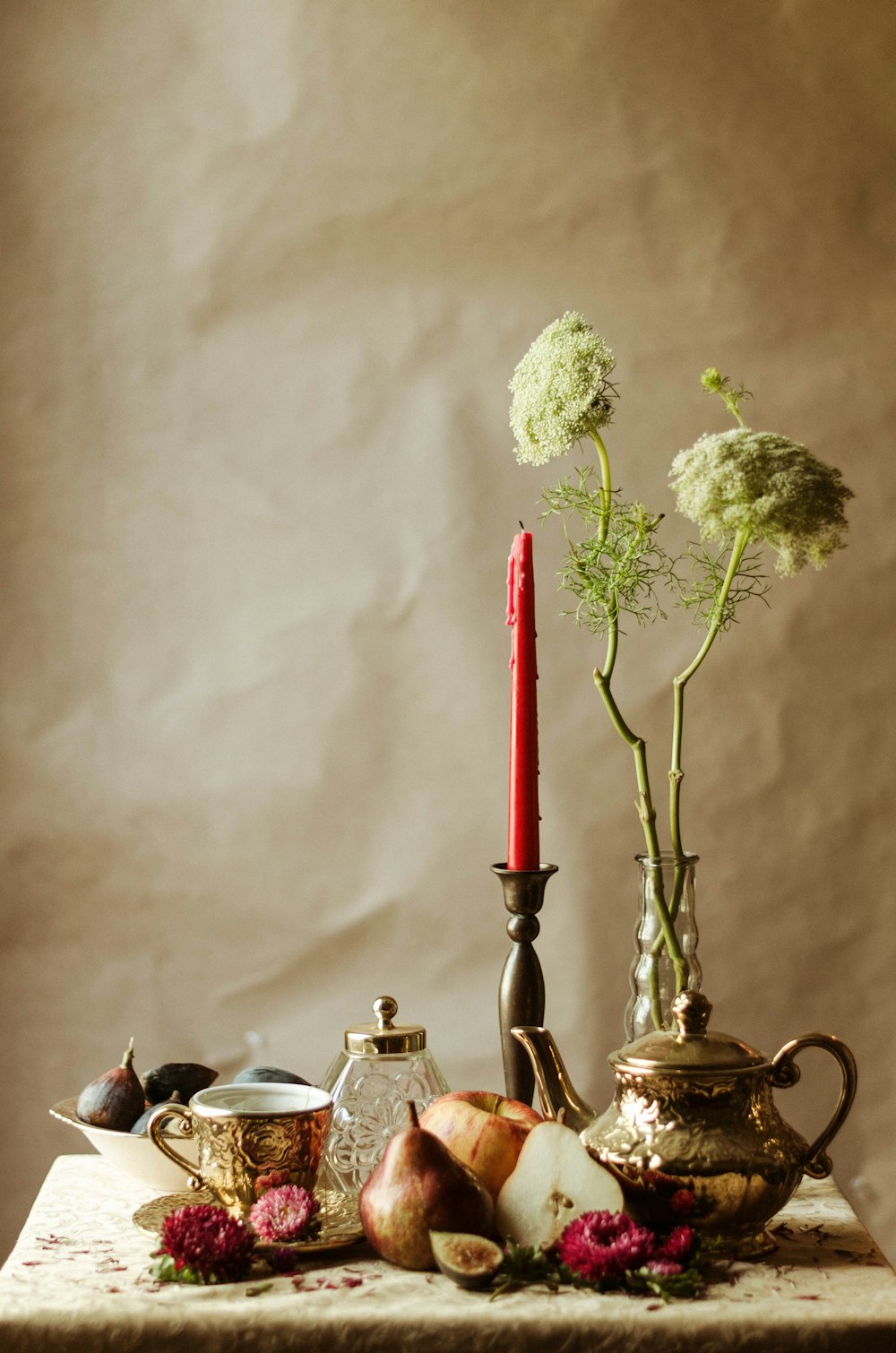 red candle in candle holder near petaled flowers and teapot