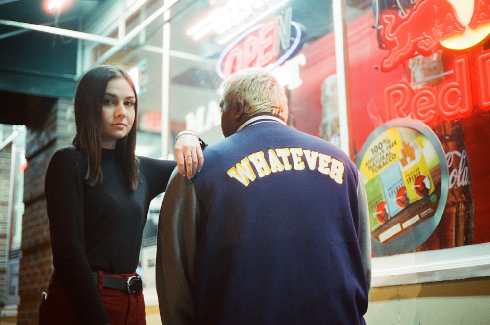 woman leaning on man in blue Whatever jacket near store