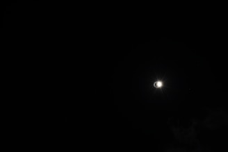 The image captures a solar eclipse against a dark sky, with a bright halo of light emerging from behind the moon, creating a striking contrast.