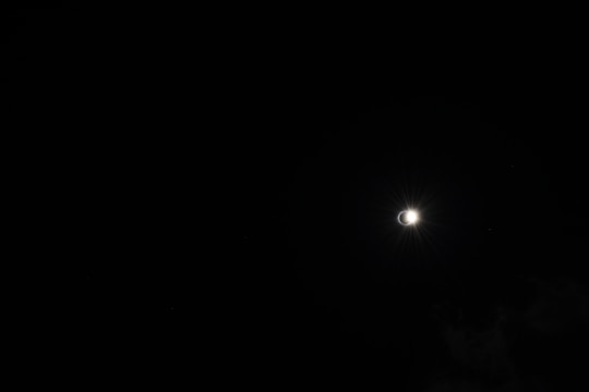 The image captures a solar eclipse against a dark sky, with a bright halo of light emerging from behind the moon, creating a striking contrast.