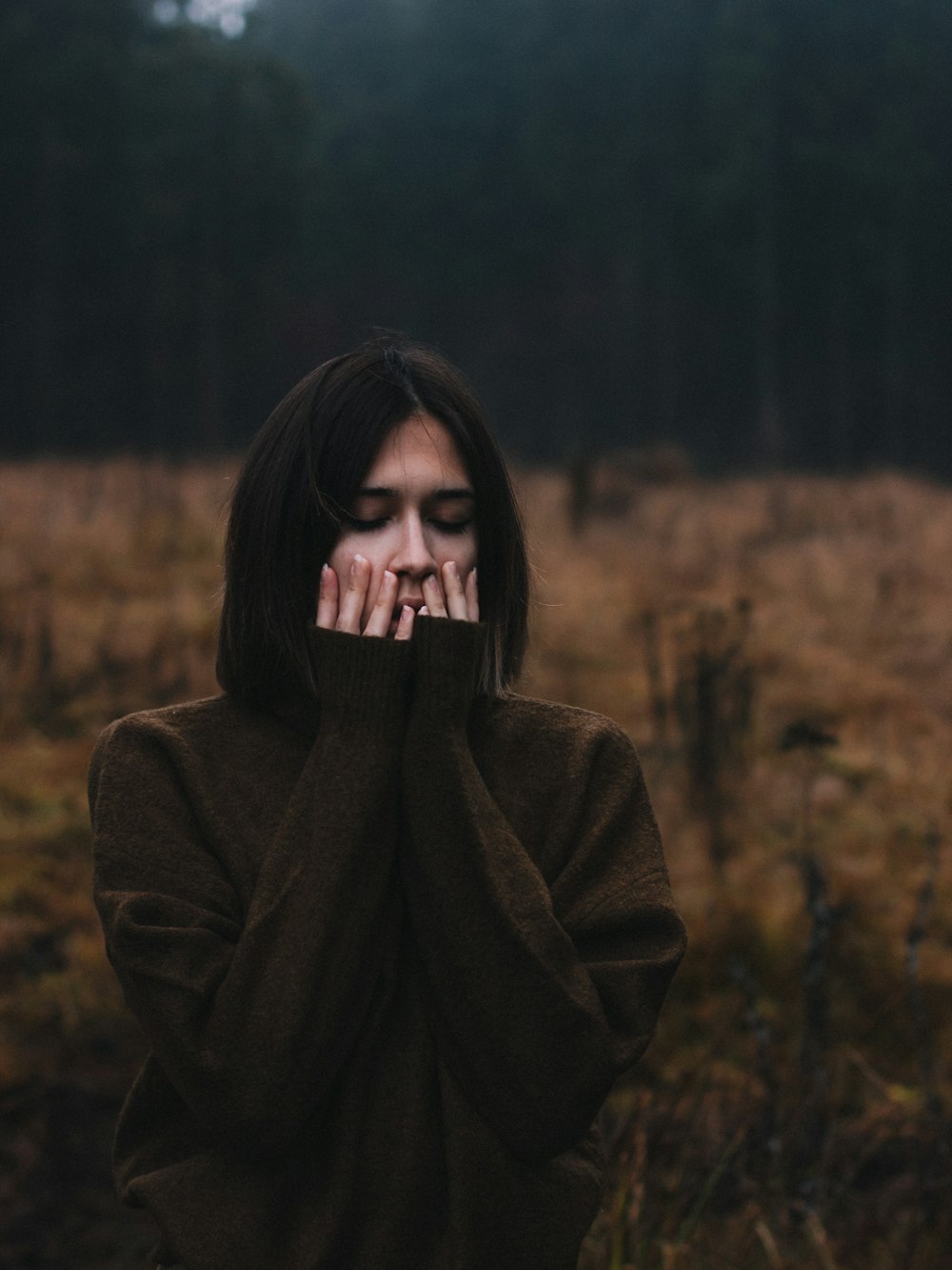 woman standing on dried grass surrounded with trees during daytime