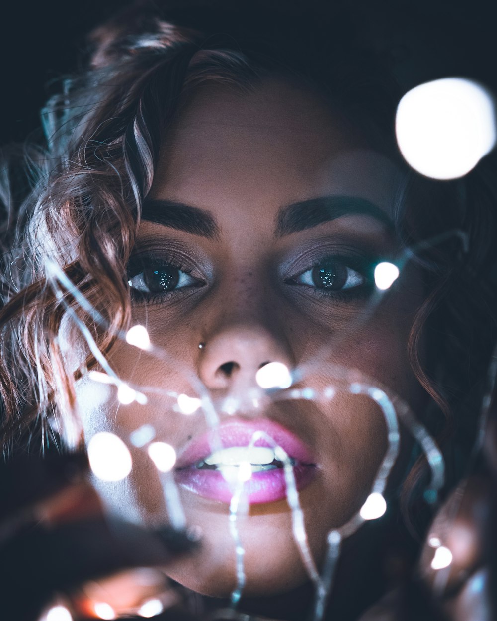 a woman holding a string of lights up to her face