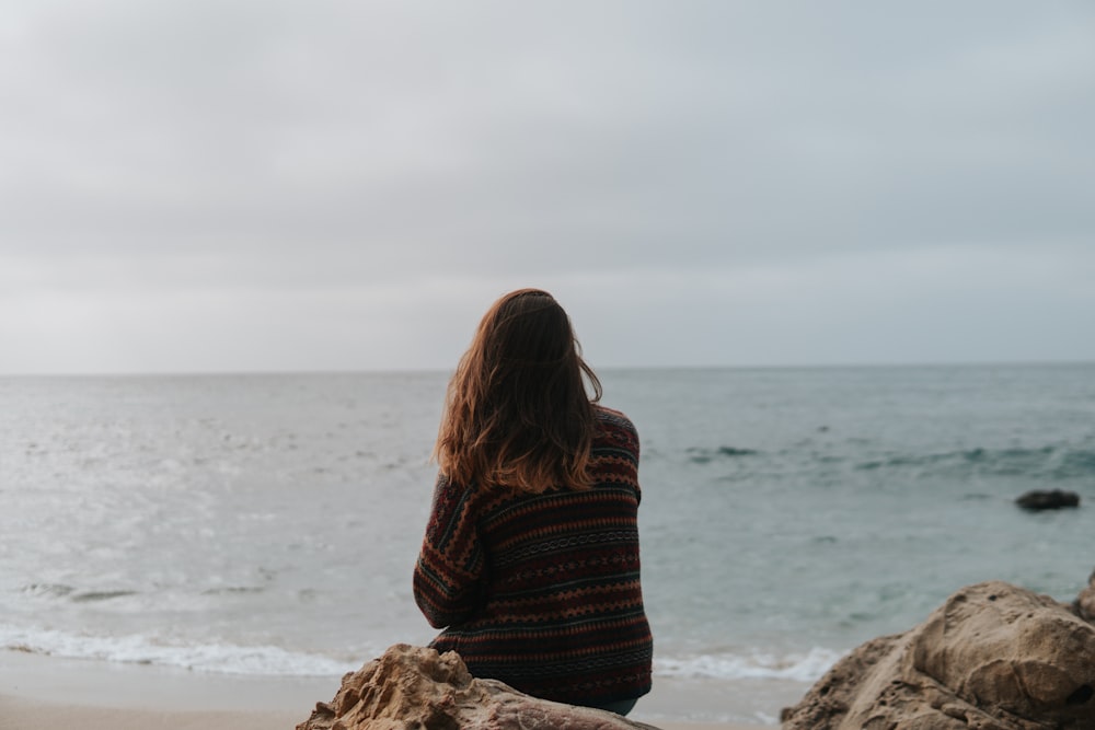 femme assise sur le rocher sur le rivage pendant la journée