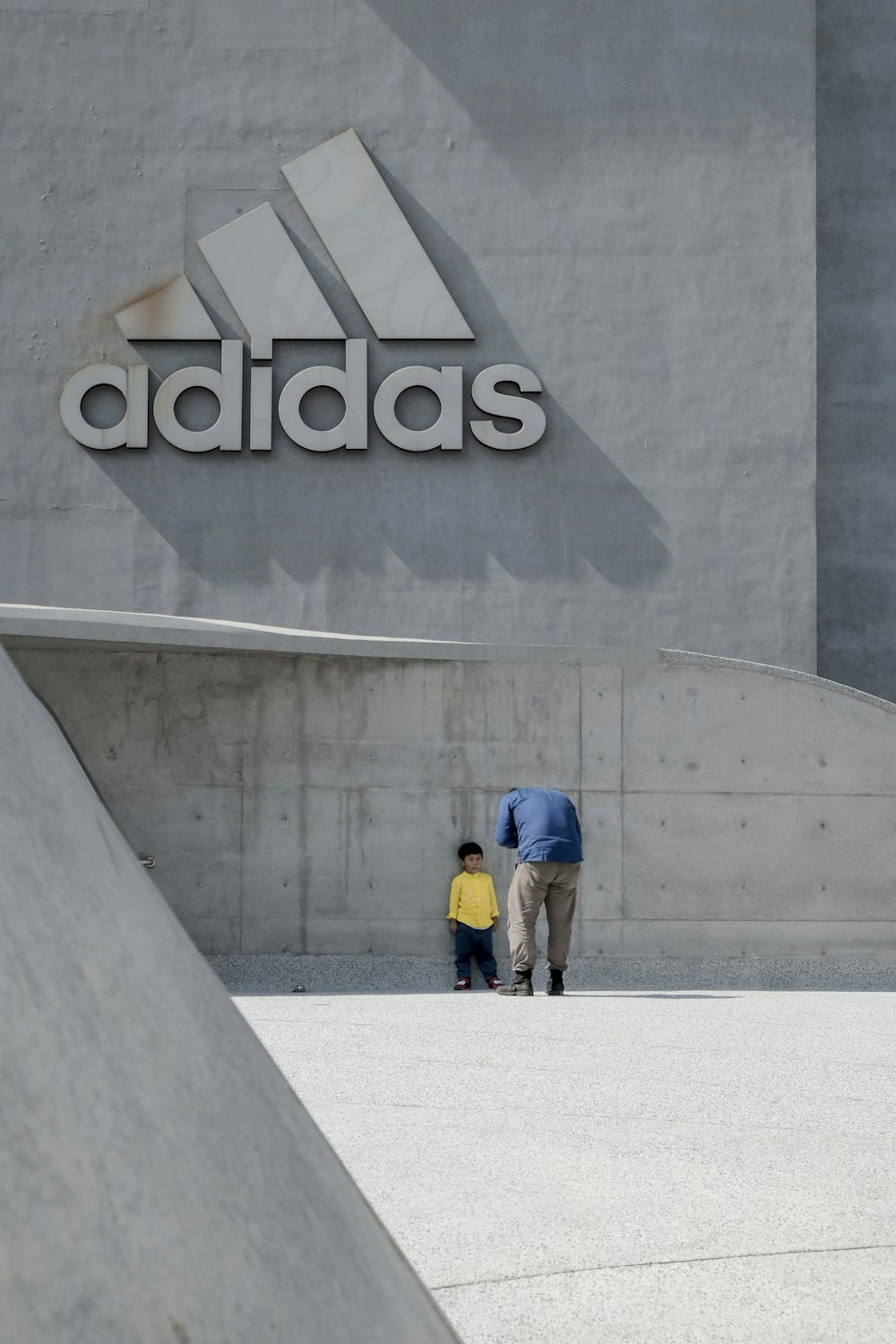 Hombre de pie frente a un niño que se apoya en la pared del edificio adidas