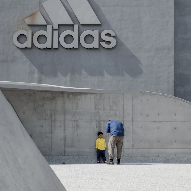 A man standing in front of a boy who is leaning on an adidas building wall