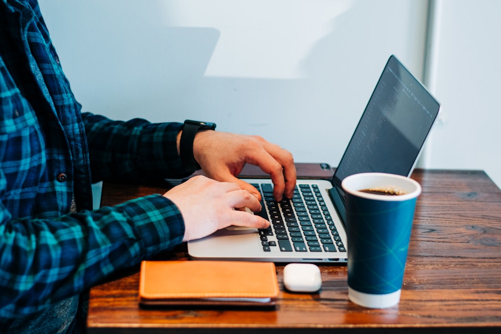 person wearing blue and green plaid collared button-up long-sleeved shirt sitting while using MacBook Pro