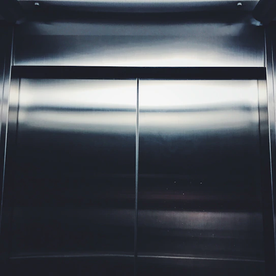 Close-up of a polished stainless steel elevator cabin door reflecting soft blue lighting.