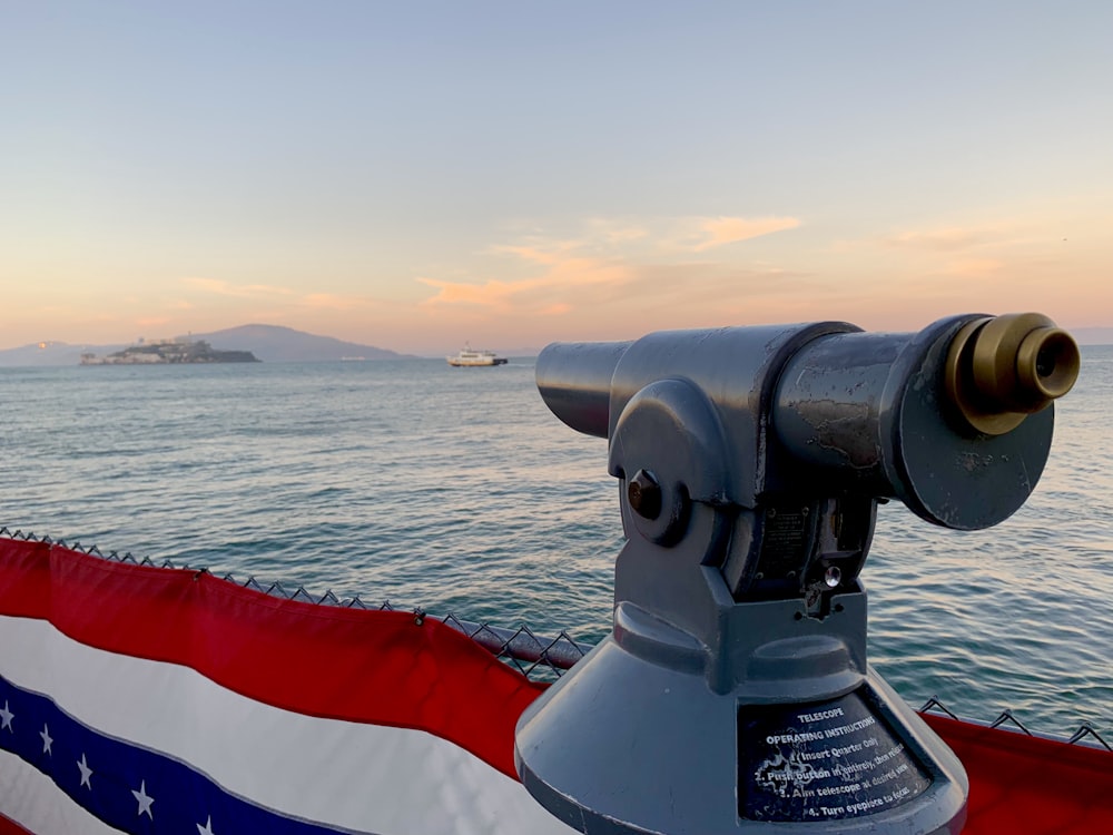 gray telescope near American flag viewing blue sea and mountain under blue and white sky