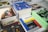A collection of books and magazines is arranged on a table, including titles such as 'Design', 'bauhaus', 'Golden Age DC Comics', and a book with an 'Adults Only' label. The covers display bold colors and graphics, featuring a variety of subjects from comics to architecture.