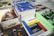A collection of books and magazines is arranged on a table, including titles such as 'Design', 'bauhaus', 'Golden Age DC Comics', and a book with an 'Adults Only' label. The covers display bold colors and graphics, featuring a variety of subjects from comics to architecture.