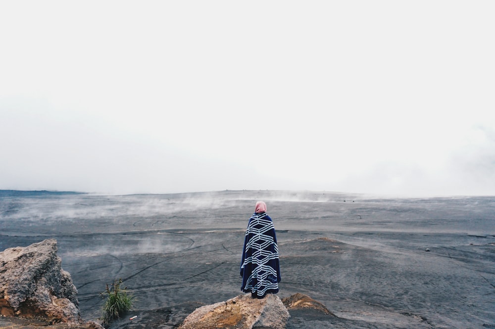 person wearing black and white dress standing on rocky hill facing on desert