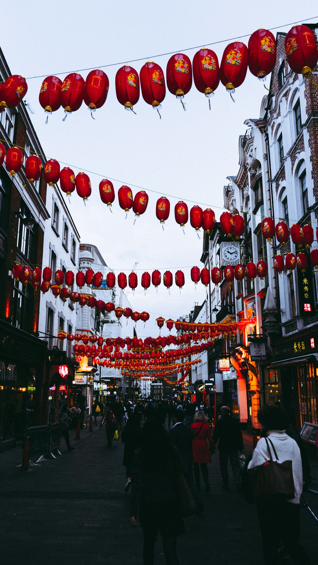 people walking between buildings under hanging Chinese lanterns during day
