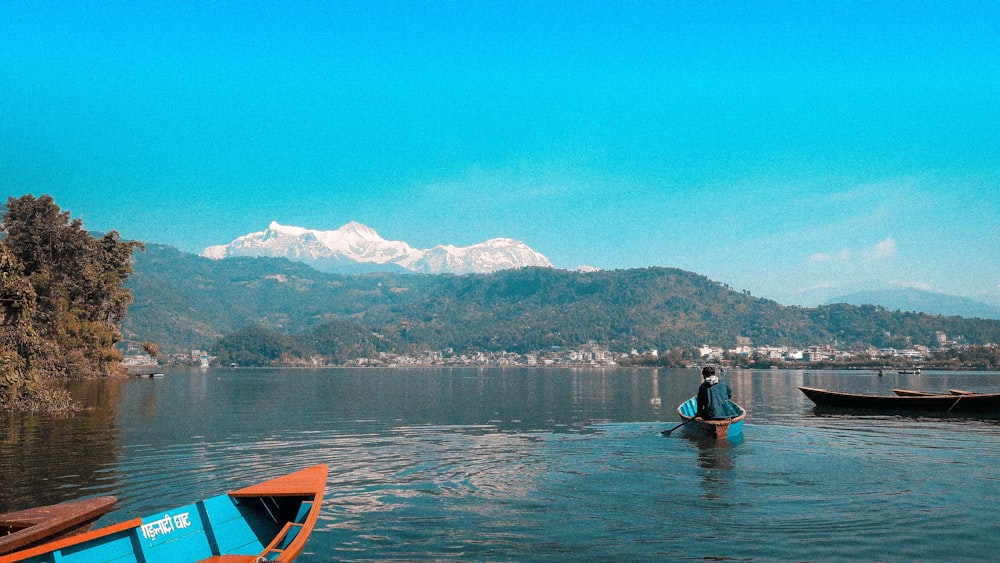 persona que monta en un bote azul en un cuerpo de agua que ve la montaña bajo el cielo azul y blanco