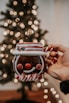 A cozy holiday scene featuring a hand holding a festive OrbitBuddies tumbler decorated with snowflakes and a custom name.