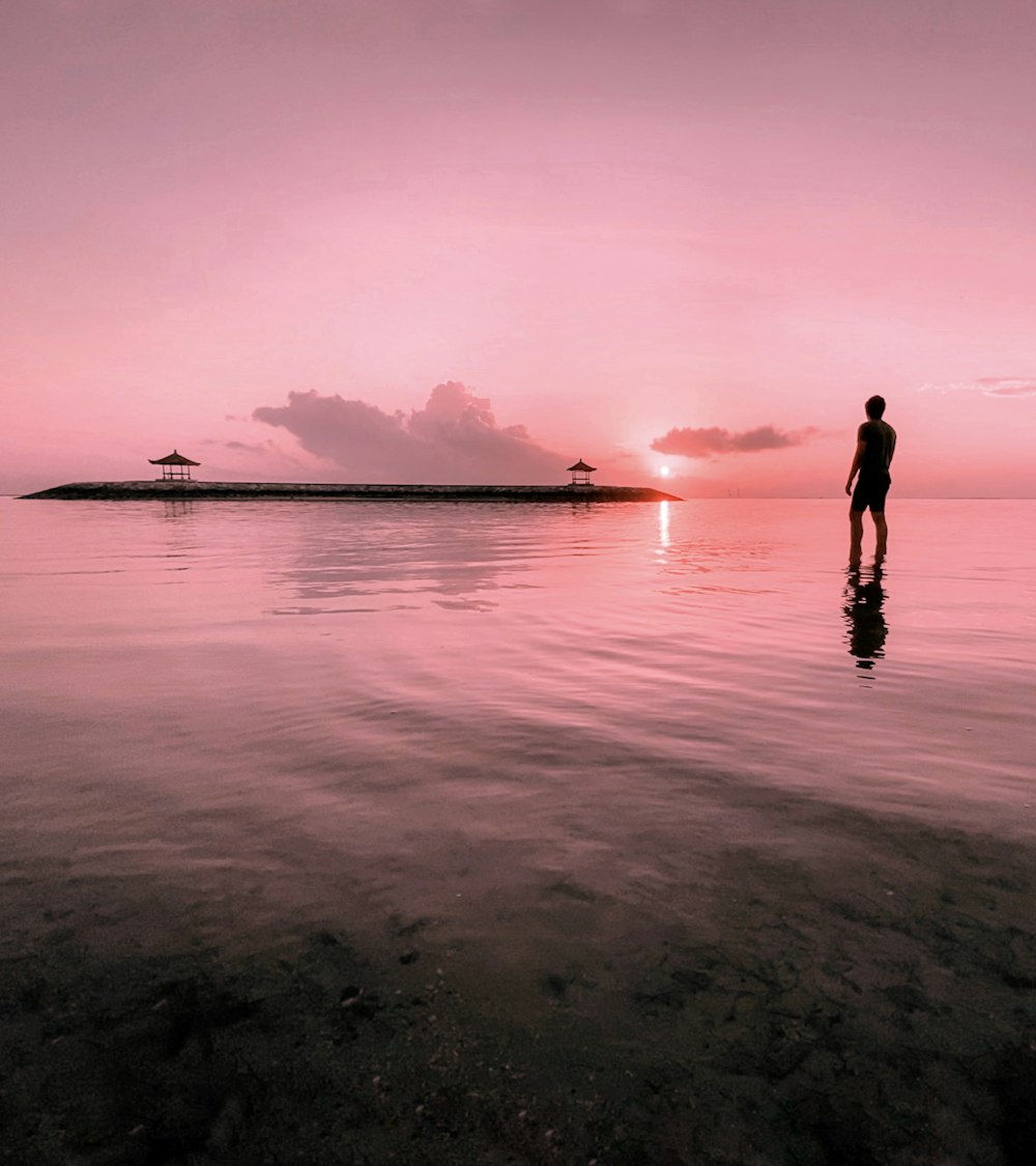 man standing on water near island during dawn