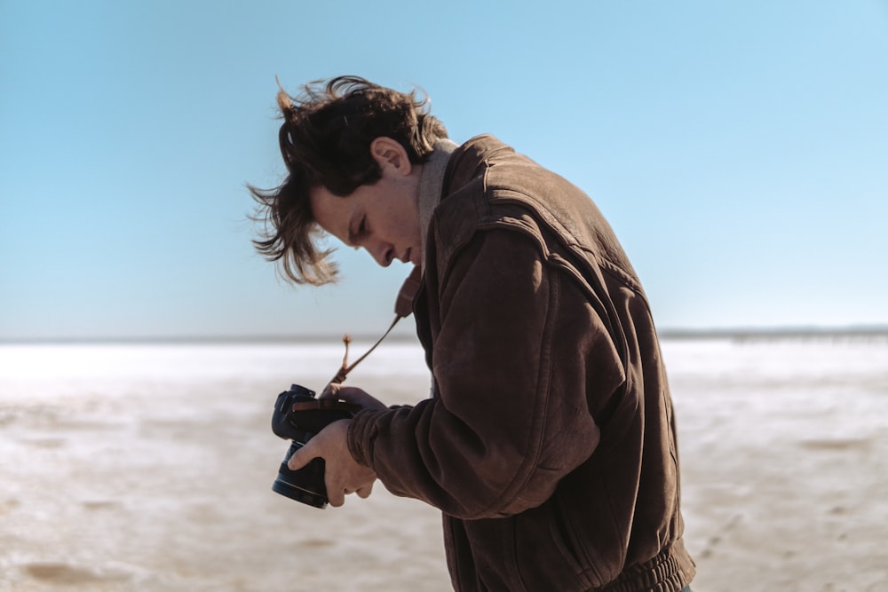 man wearing brown jacket holding DSLR camera