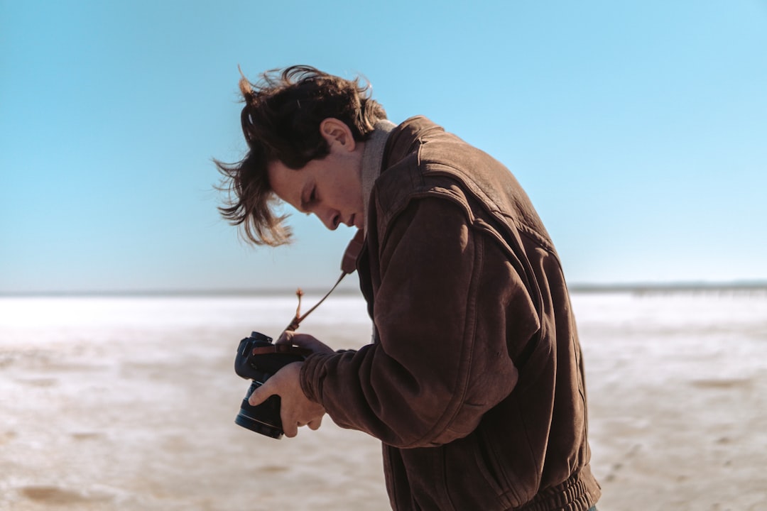 man wearing brown jacket holding DSLR camera