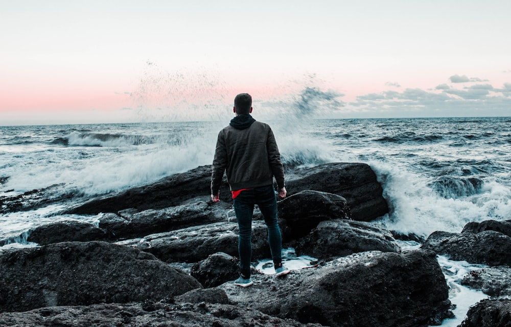 a man standing on top of a rocky beach next to the ocean