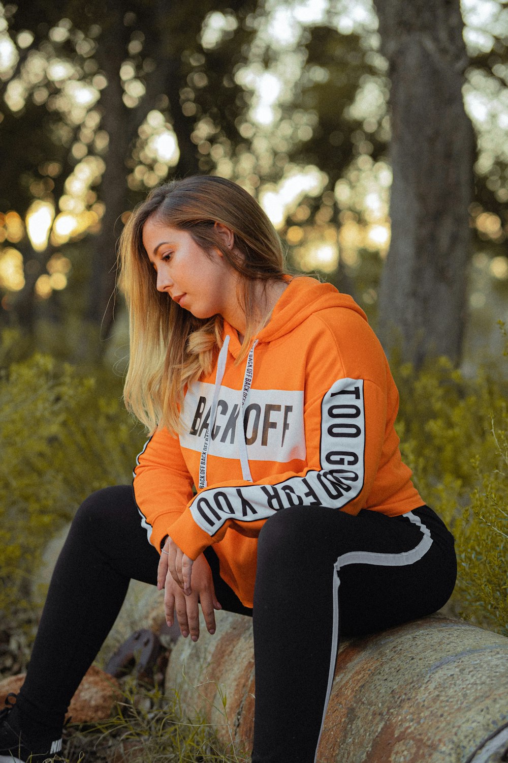 woman in orange and white pullover hoodie and black leggings sitting on stone during daytim