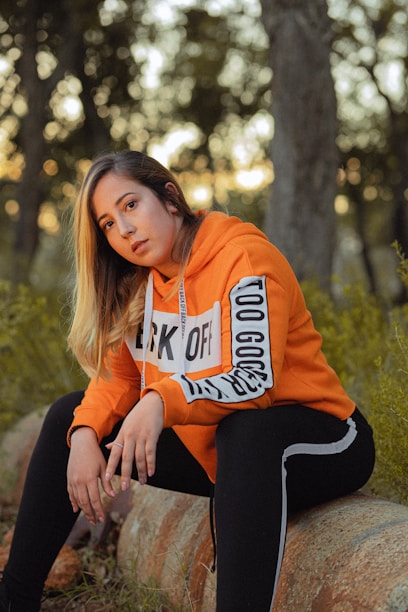 woman sitting on log in orange hoodie