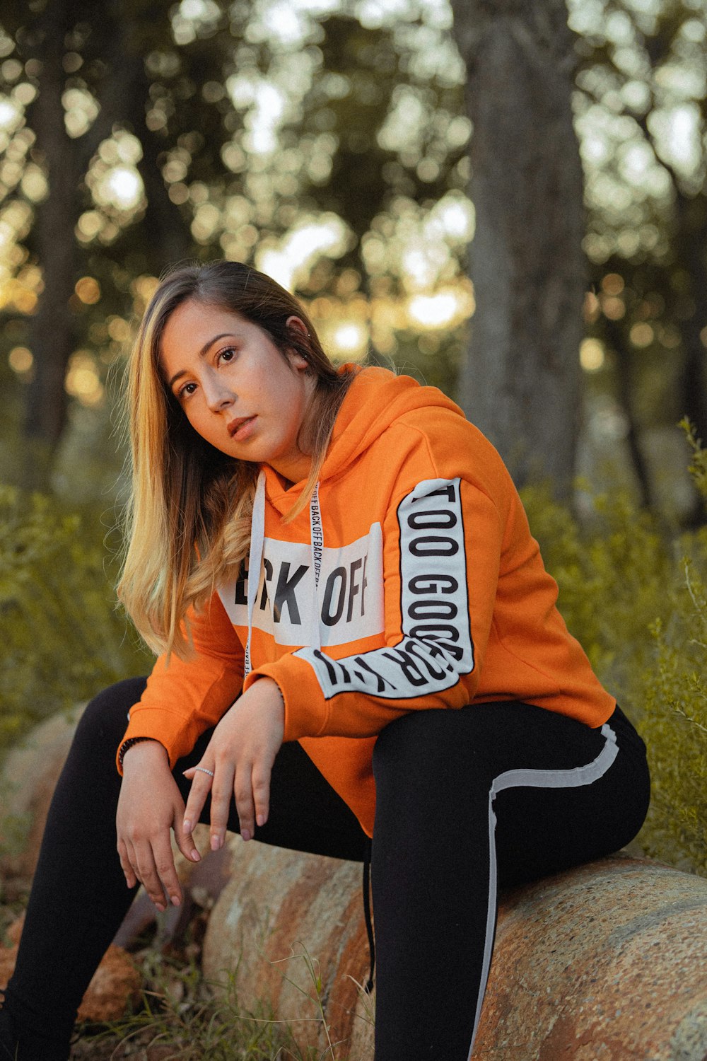 woman sitting on log in orange hoodie