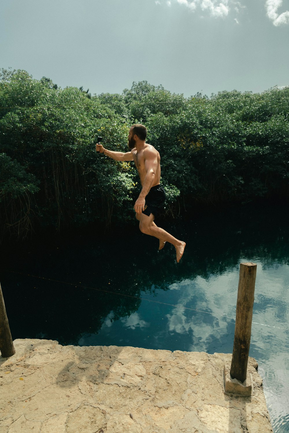 man wearing black board shorts jumping on lake