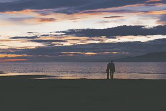 A companion and client sharing a sunset view on a beach, wrapped in warm light and soft smiles.
