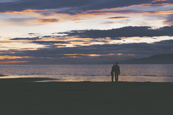 A companion and client sharing a sunset view on a beach, wrapped in warm light and soft smiles.